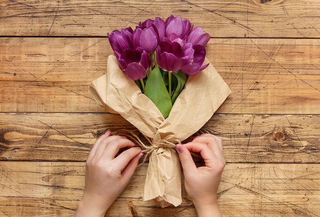 Handen wikkelen paars tulpenboeket in papier over houten tafel
