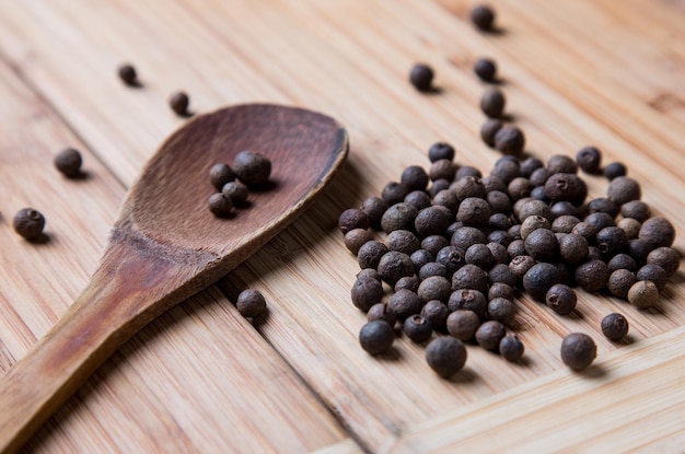 Handful of allspice pepper with a wooden spoon on the bamboo board