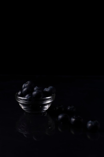 A handful of blueberries in a glass bowl on a black background