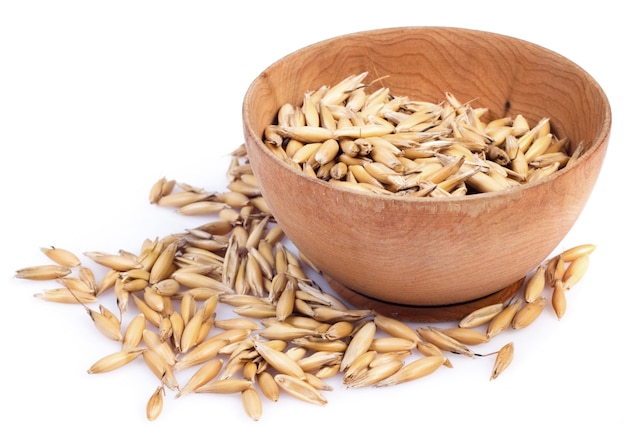 Photo handful of crops of oats in the wooden saucer on a white surface