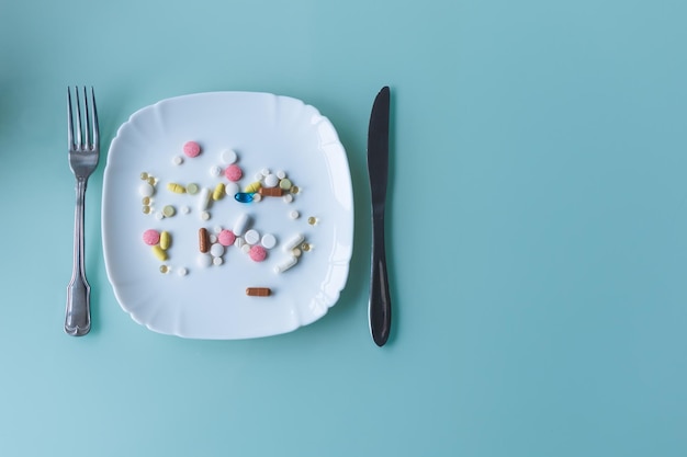 A handful of pills capsules and multicolored tablets on a plate next to cutlery Taking medication Pills instead of food The concept of vitamins instead of food