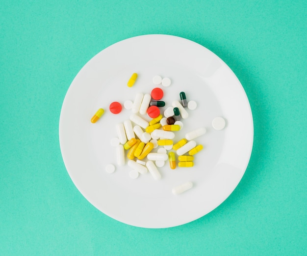 Handful of scattered medicines, pills and tablets on white plate on blue background