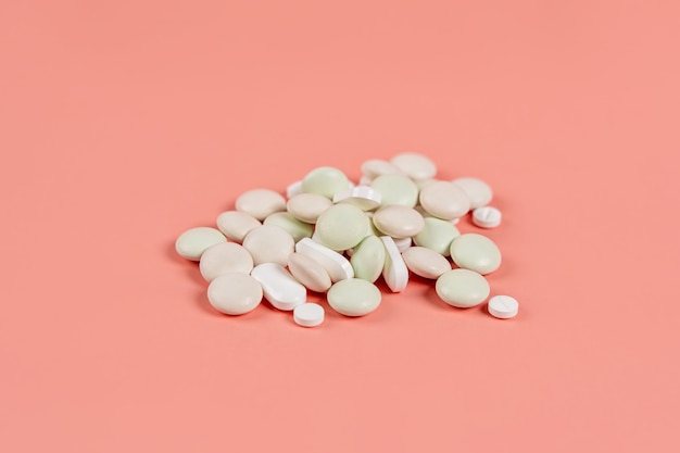 A handful of tablets and capsules on a pink background