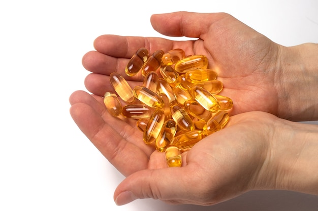 A handful of yellow omega-3 capsules in human hands.