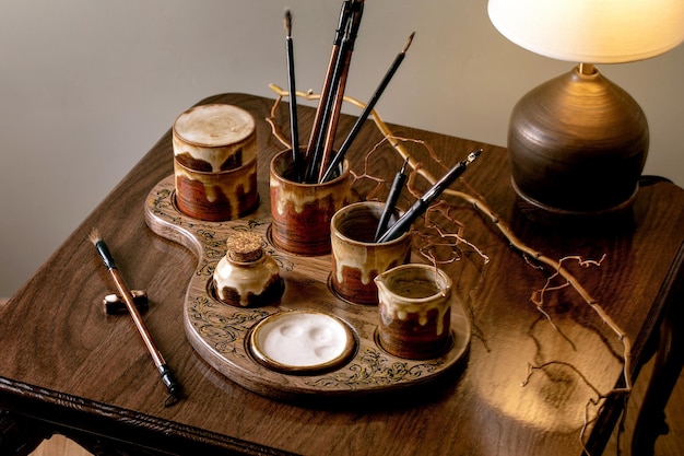 Handgemaakte keramische set voor schilderen en kalligrafie op stijlvolle houten stoel Borstels kalligrafie pennen palet inkten op houten tafel met warm tafellamp licht Kunstenaar kunst en hobby