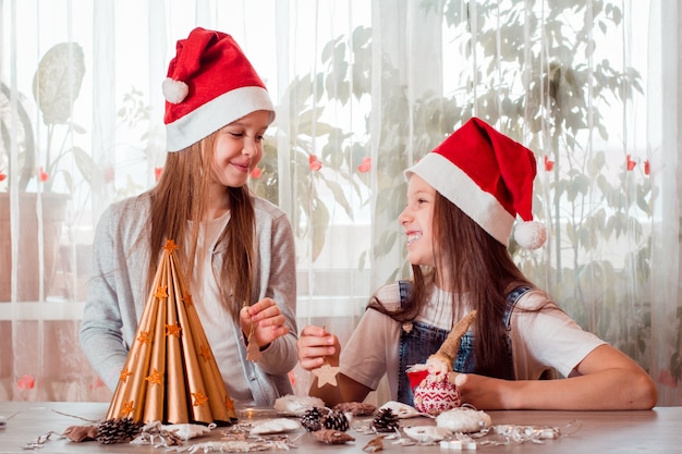 Handgemaakte kerst. De meisjes lachen en staan op het punt een zelfgemaakte kerstboom te versieren met houten speelgoed