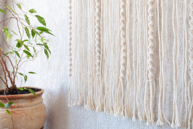 Handgemaakte macramé muurhanger 100 katoenen wanddecoratie met houten stok hangend aan een witte muur Macrame vlechten en katoenen draden Vrouwelijke hobby ECO vriendelijk modern concept in het interieur