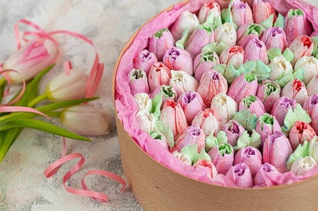 Handgemaakte marshmallows in houten verpakkingen op een lichte achtergrond met bloemen. Het concept van de feestdagen Vrouwendag en Valentijnsdag.