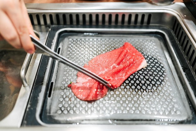 Handgrillen van een medium zeldzaam stuk Kagoshima Wagyu A5-rundvlees met marmertextuur met een tang gegrild op een metalen yakiniku-pan Geserveerd voor Yakiniku