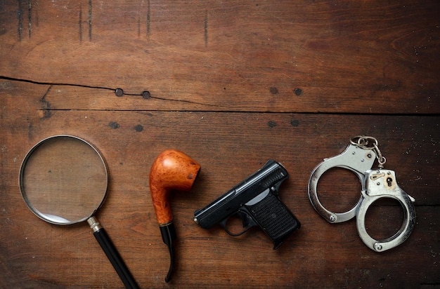 Handgun handcuffs and a smoking pipe on wooden background