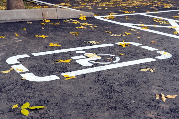 Handicapped disabled people parking lot sign drawing with white lines on the asphalt. Yellow autumn leaves in the parking lot