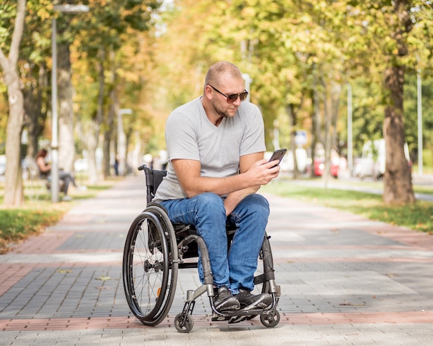 Uomo disabile in sedia a rotelle al vicolo del parco utilizza uno smartphone