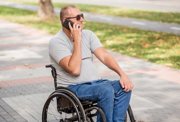 Handicapped man in wheelchair at the park alley use a smartphone