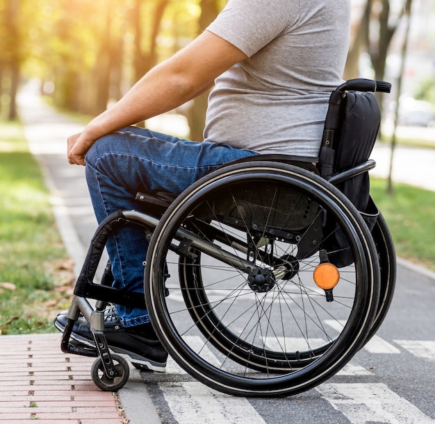 Uomo disabile in sedia a rotelle si prepara ad attraversare la strada sul passaggio pedonale