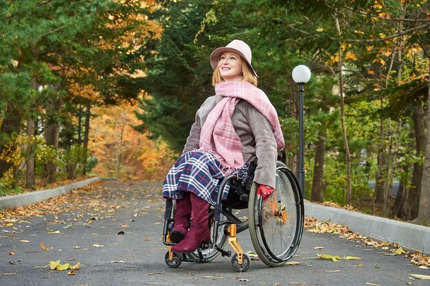 Donna sorridente paralizzata handicappata in sedia a rotelle si muove nel parco d'autunno