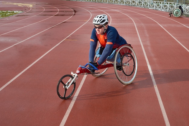 Photo handicapped sportsman in helmet and sunglasses sitting in racing wheelchair at outdoor track and field stadium and getting ready for marathon