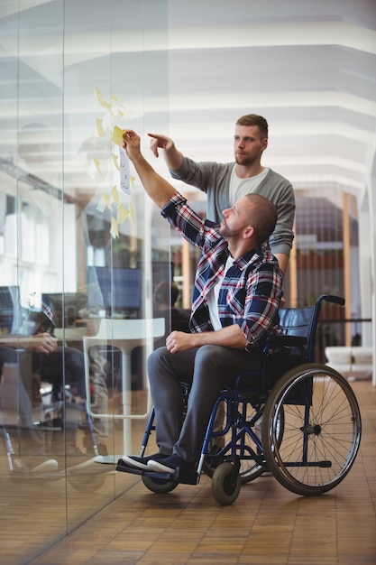 Foto handicapzakenman met collega die zelfklevende nota's in bureau plakken