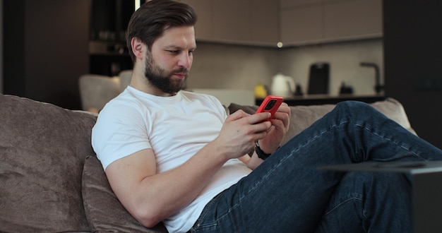 Handige baarde man gebruikt telefoon zit thuis op de bank scrollt en kijkt thuis naar sociale media mensen lifestyle concept