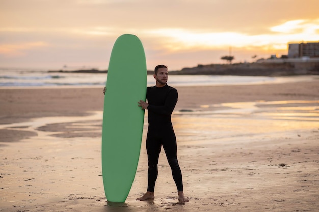 Handige surfer man met zijn surfplank op het strand bij zonsondergang