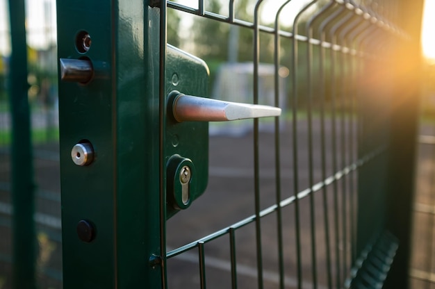 Handle with a lock on the open gate of a sports ground fenced\
with a welded mesh fence