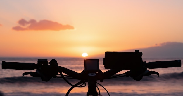 Handlebar silhouette of an electric bicycle parked along the sea in the sunset light