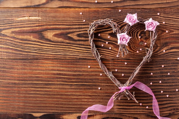 Handmade branches heart with flowers and pink ribbon on wood