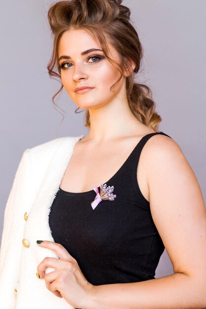 a handmade brooch in the form of a bouquet of lilac flowers on a black tshirt of a brunette girl the girl is posing on a gray background smiling and looking at the camera