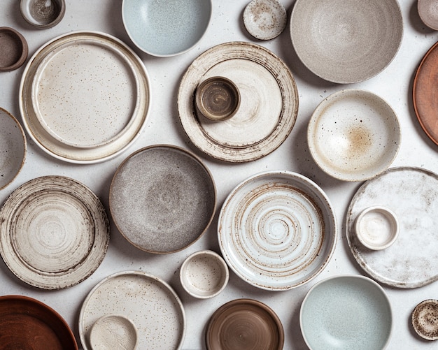 Handmade ceramics, empty craft ceramic plates and bowls on light background, top view