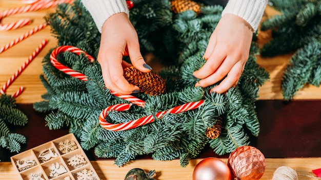 수제 크리스마스 인테리어 장식. 녹색 전나무 나무 나뭇 가지, 사탕 지팡이를 사용 하여 화 환을 만드는 여성 꽃집 손의 근접 촬영.