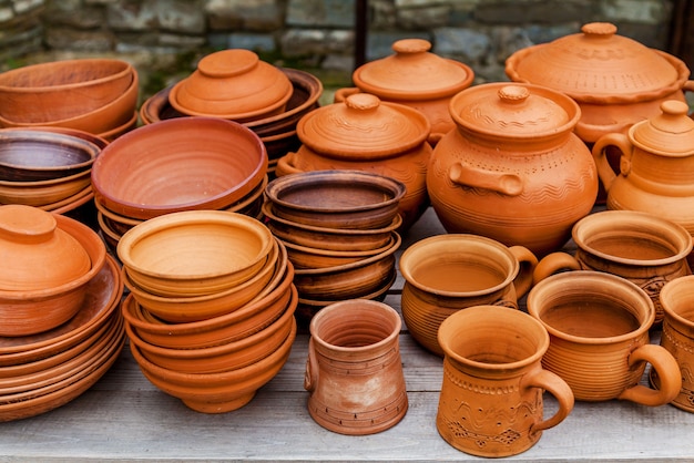 Handmade clay brown cups, pots and plates on a wooden stand