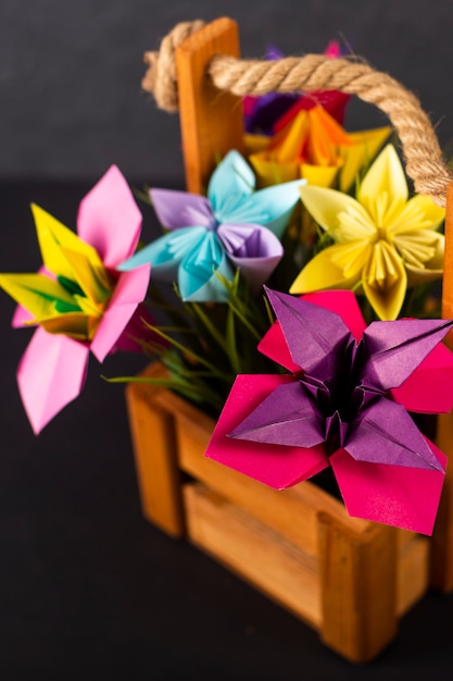 Foto arte fatta a mano del mestiere di carta del mazzo di origami dei fiori di carta colorata in un canestro con erba nello studio sulla macro colorata del primo piano del fondo