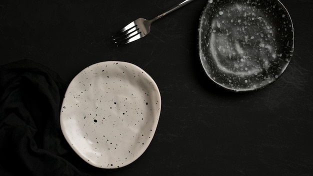 Handmade craft ceramic plates set with fork on black\
background. ceramic crockery. top view