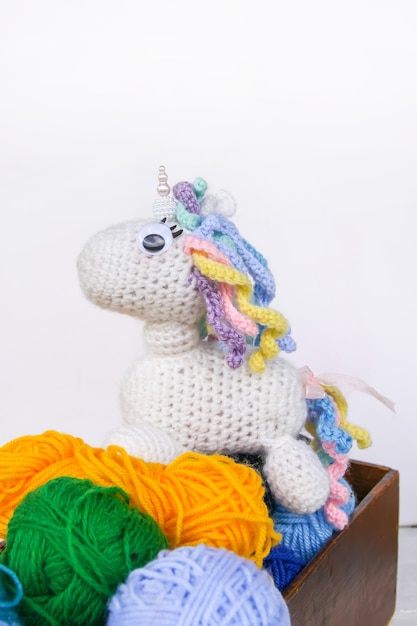 Handmade crocheted unicorn toy and colorul yarn in a wooden box on white background.