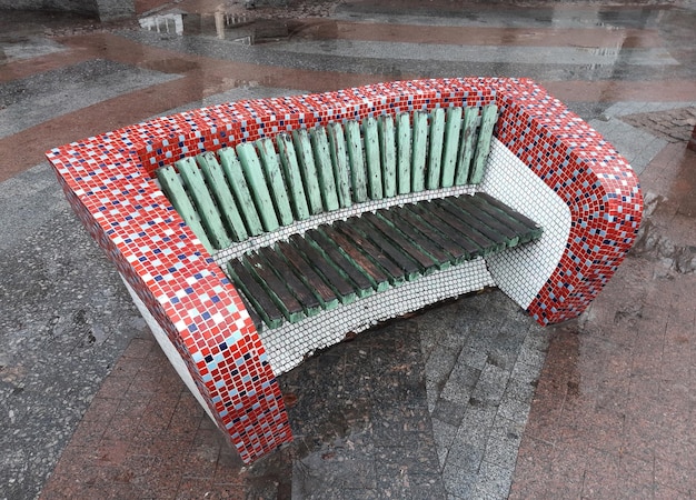 Handmade decorative bench covered with bright mosaic tiles. On the concrete sidewalk