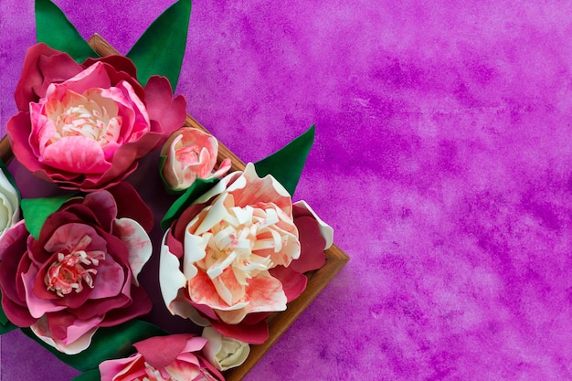 Handmade decorative peonies made from foamiran on wooden panel on the purple background