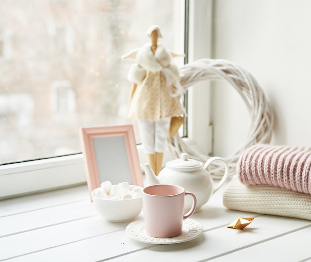 Handmade doll with tea set and marshmallows near window. Cozy winter morning breakfast. Christmas concept and mood. 
