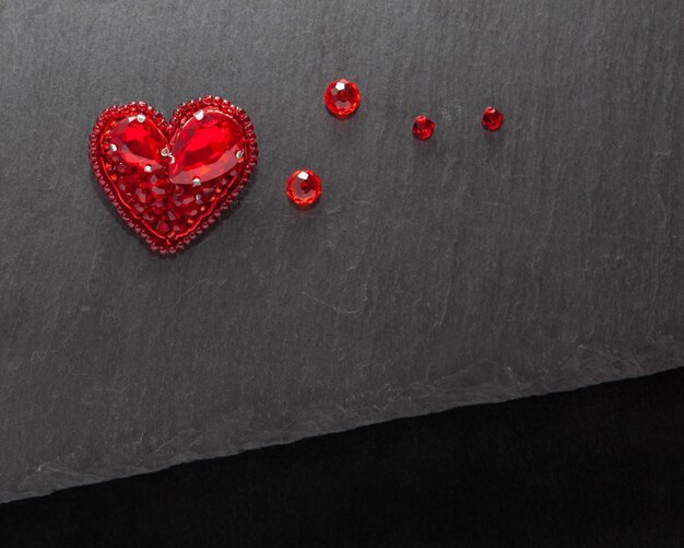 Handmade embroidered red heart brooch on dark stone background top view with empty place for text