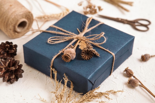 Handmade gift box in dark blue packaging poppy seed heads dried flowers on white desk Gift for man Floristic herbarium craft Natural colours