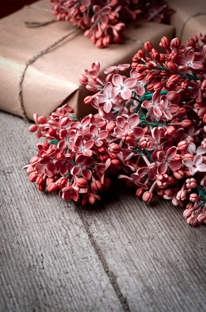 Handmade gift boxes wrapped with craft brown paper, decorated with fresh purple lilac flowers on a vintage wooden surface.