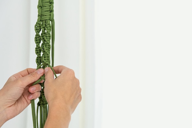 Handmade green macrame plant hangers with potted plant are hanging on woman hand. The macrame have pot and monstera plant inside them.