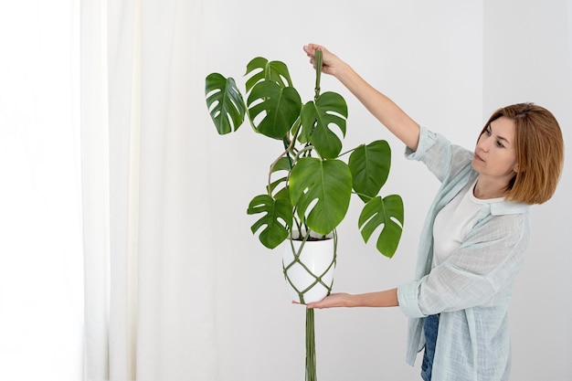 Handmade green macrame plant hangers with potted plant are hanging on woman hand. The macrame have pot and monstera plant inside them.