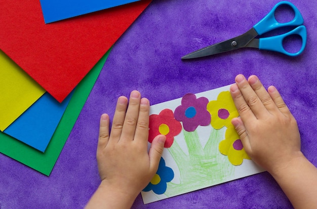 Handmade greeting card with flowers in child hands on the purple background