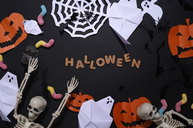 Handmade Halloween decor and skeleton, gummy worms on black background with word Halloween. Top view. Flat lay