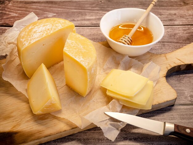 Handmade hard cheese. Natural farm cheese on an old wooden board with honey in a cup