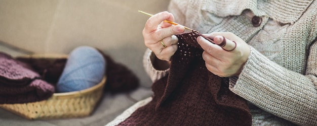 Handmade hobby stay home concept, Happy asian old woman knit brown scarf crochet and tablet on sofa in living room at home