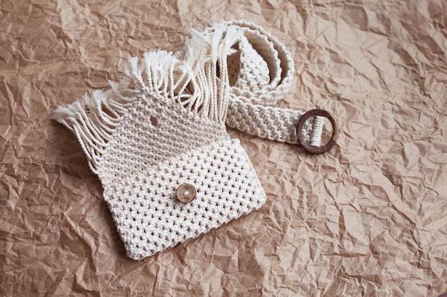 Handmade macrame belt bag on craft paper background eco\
friendly natural macrame cotton waist bag hobby knitting handmade\
macrame modern summer concept copy space