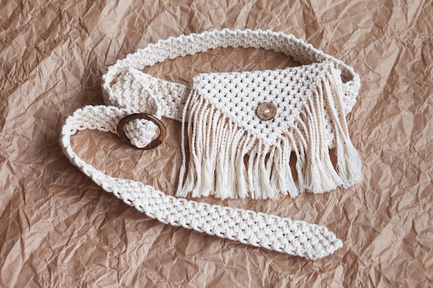 Handmade macrame belt bag on craft paper background ECO friendly natural macrame cotton waist bag Hobby knitting handmade macrame Modern summer concept