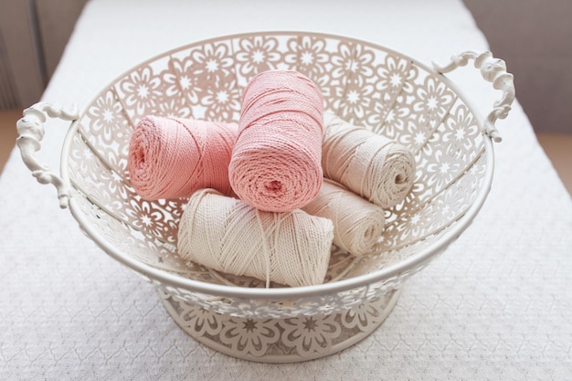 Handmade macrame braiding and cotton threads in basket on white background