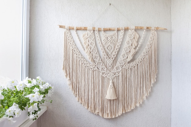 Handmade macrame decoration with wooden stick hanging on a white wall