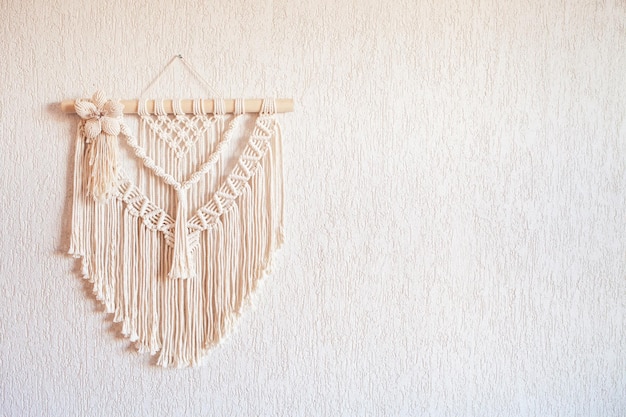 写真 白い壁に木の棒がぶら下がっている手作りのマクラメの壁の装飾マクラメの編み込みと綿の糸女性の趣味ecoフレンドリーなモダンな編み物インテリアの自然な装飾コピースペース